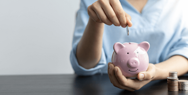 ピンクの豚の貯金箱に小銭を入れる女性
